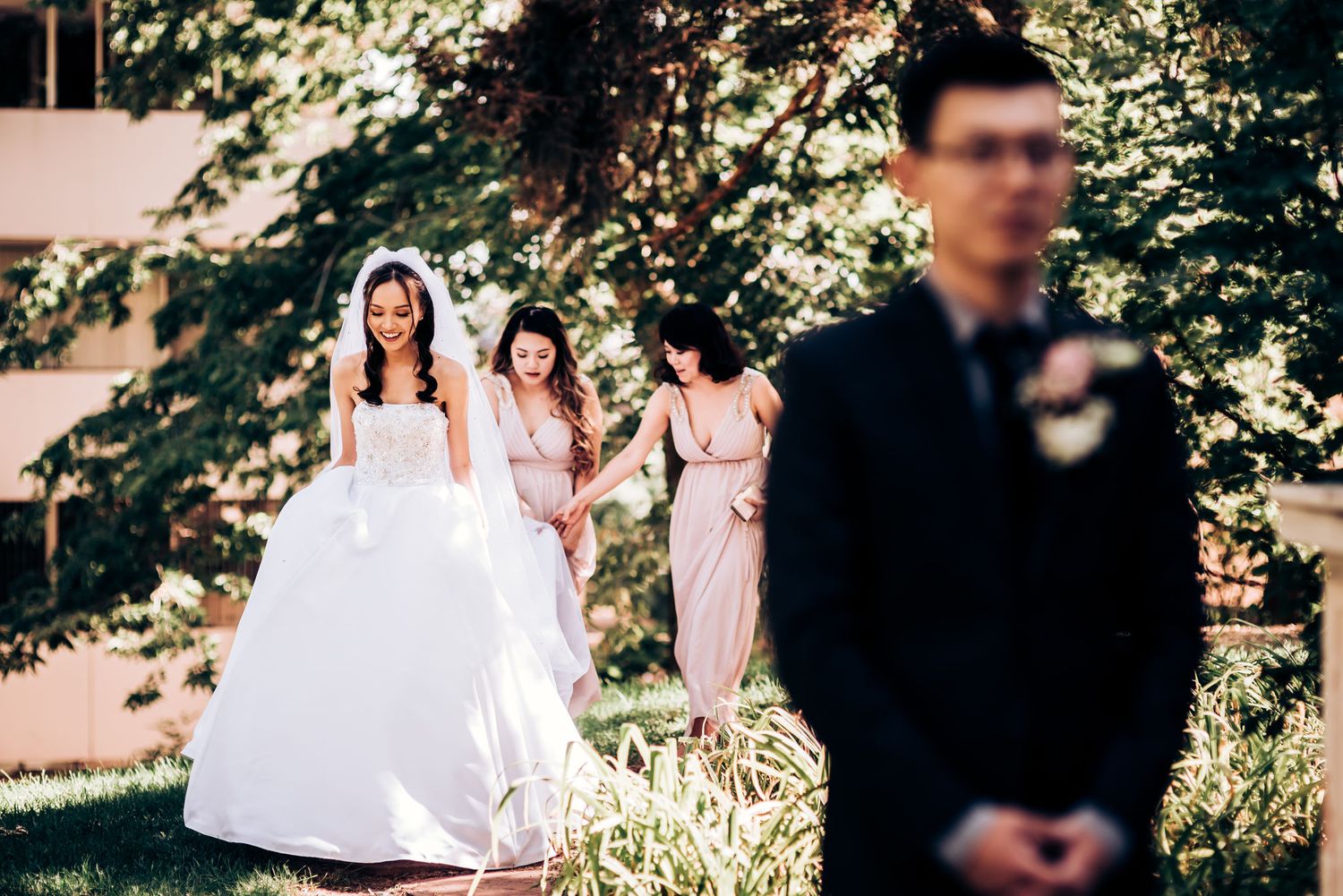 A wedding party positioned in a garden with sunlight filtering through trees.