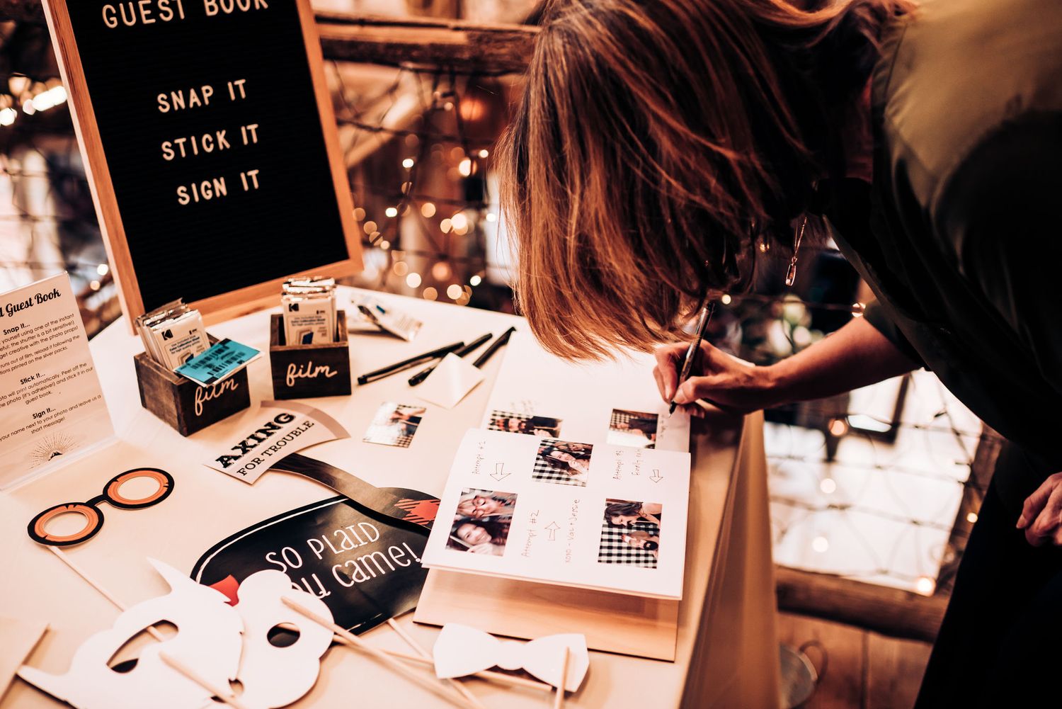 Someone signing a wedding guest book surrounded by photos and decorative items.