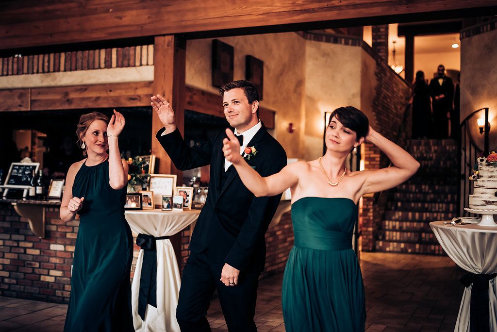 Wedding party performs synchronized dance moves at reception in elegant industrial venue.