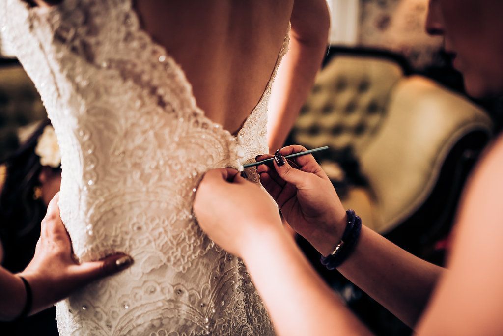 Close-up of hands buttoning up an intricate lace wedding dress with delicate details.