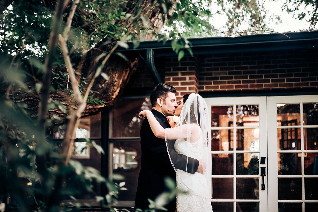 A tender wedding embrace photographed outside a charming brick building with windows.