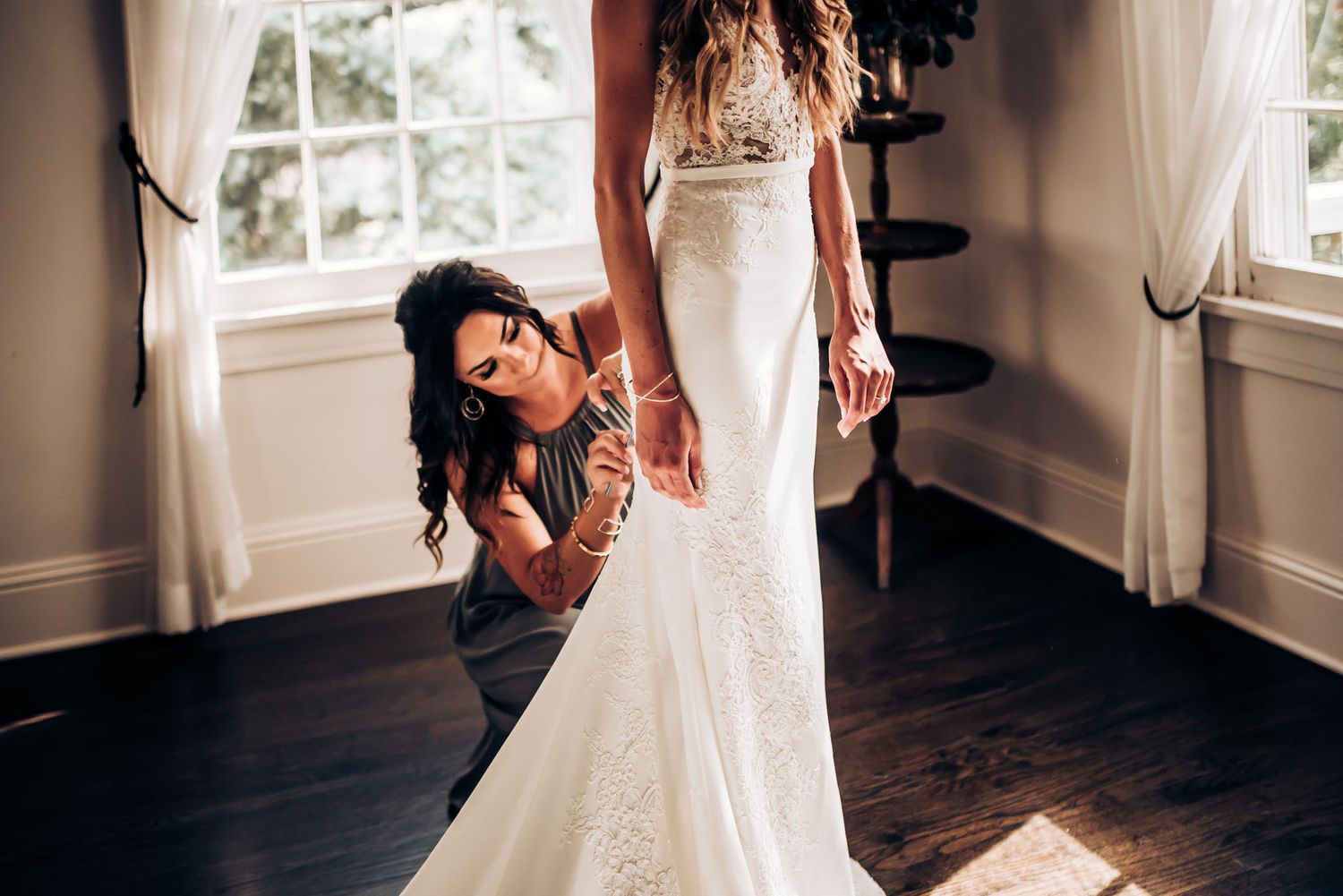 Helper adjusts details of bride's fitted lace wedding gown.