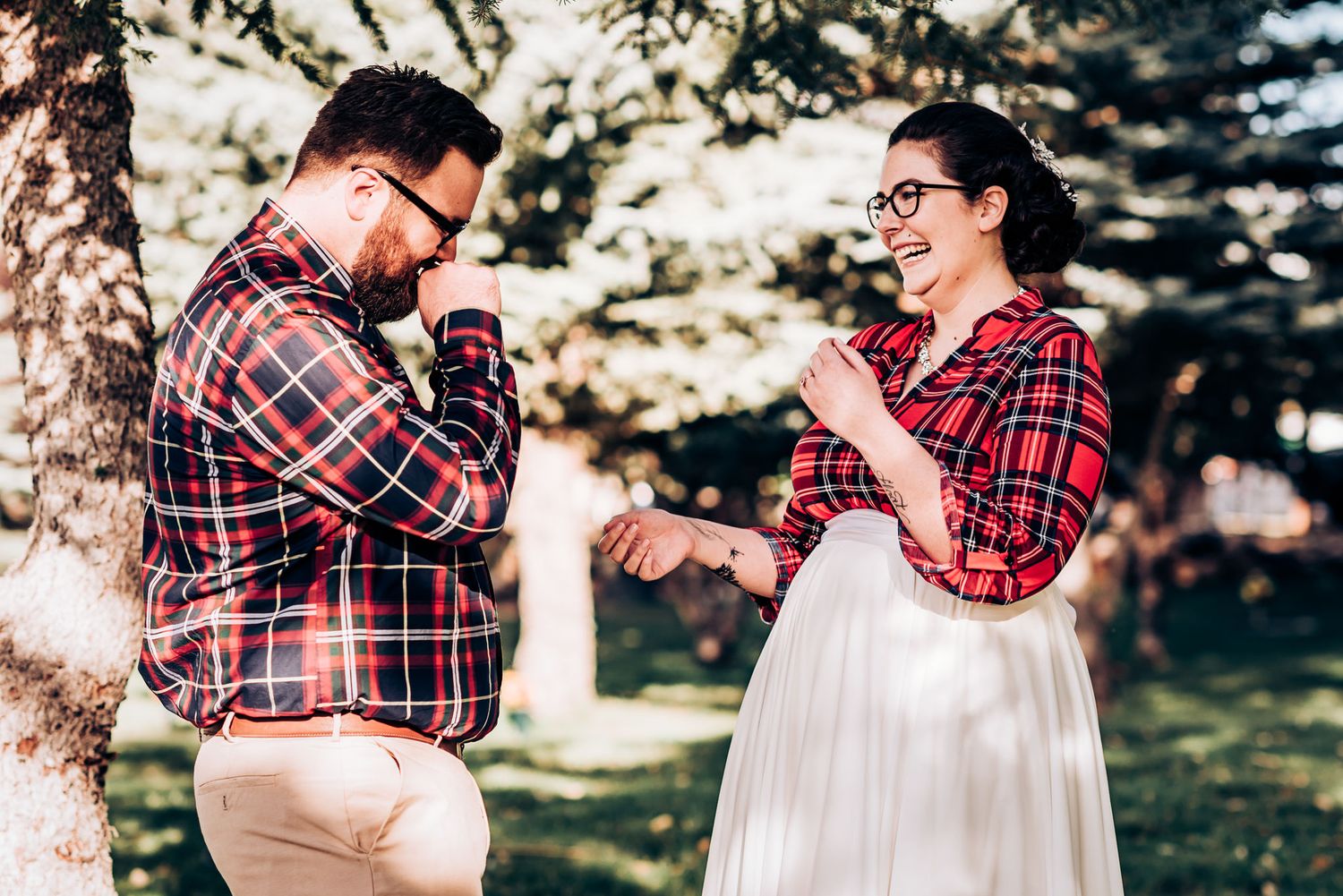 Couple in coordinating plaid outfits sharing a joyful moment by a tree.