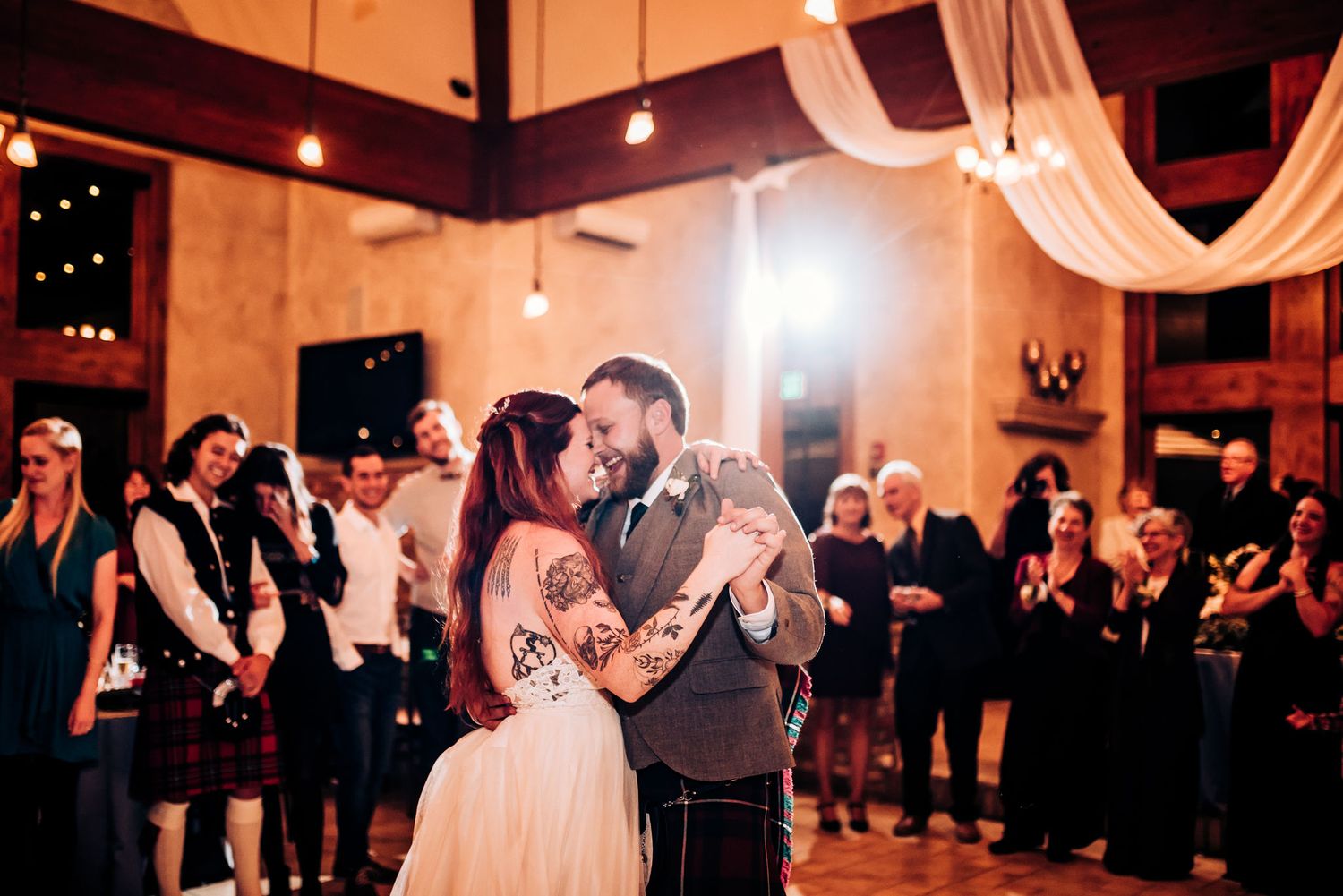 Couple embraces during romantic dance at dimly lit wedding reception.