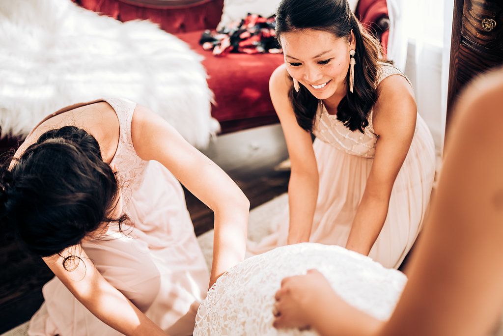 Wedding preparation moment showing final dress adjustments in natural light.