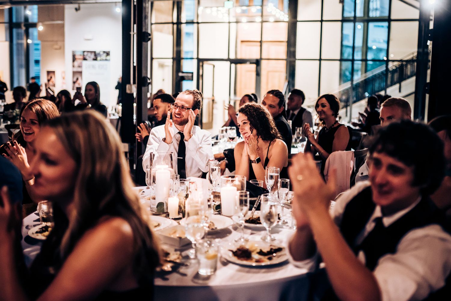 Wedding reception guests enjoy dinner and conversation in modern venue with ambient lighting.