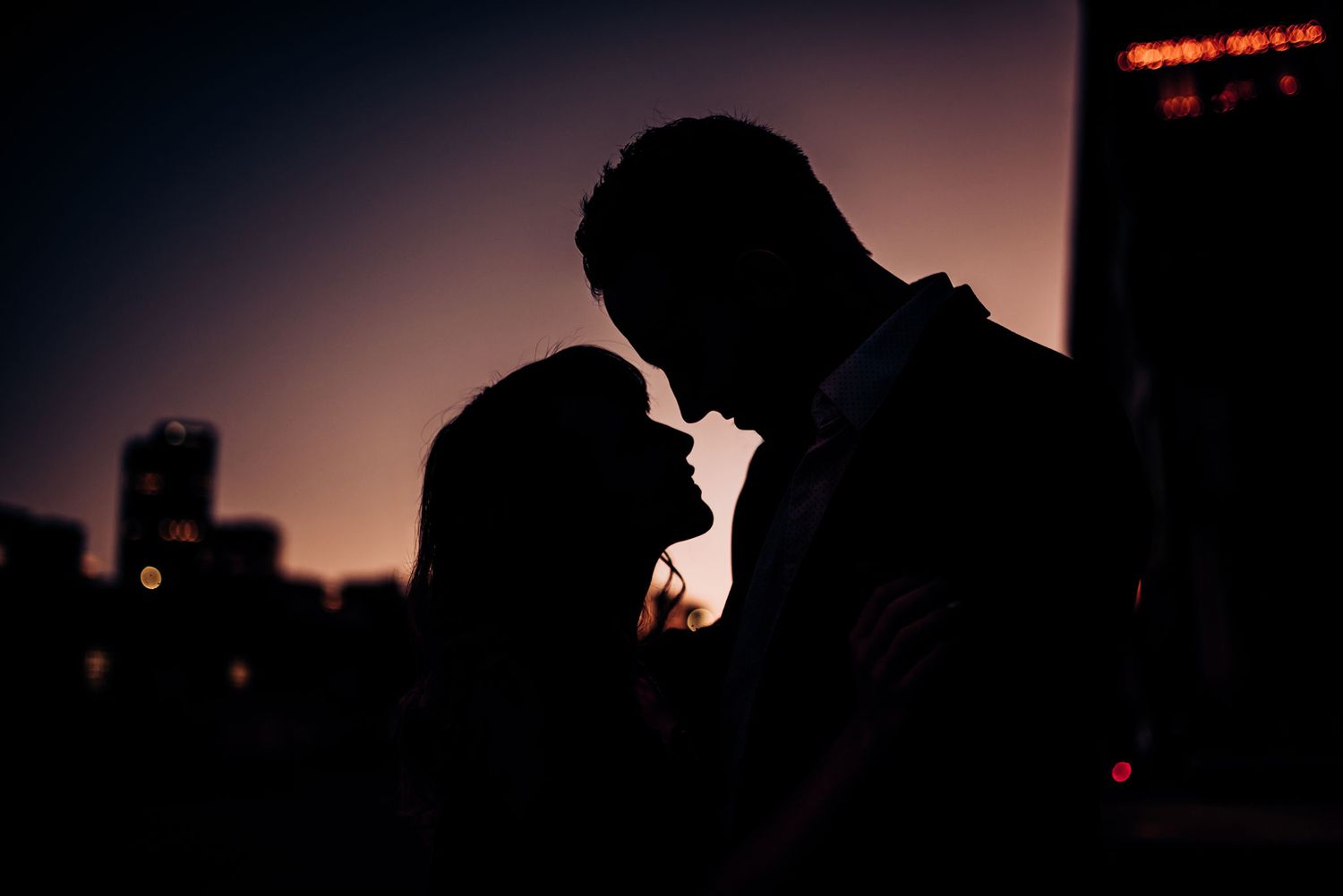 Silhouetted couple in an intimate moment against an urban sunset backdrop.