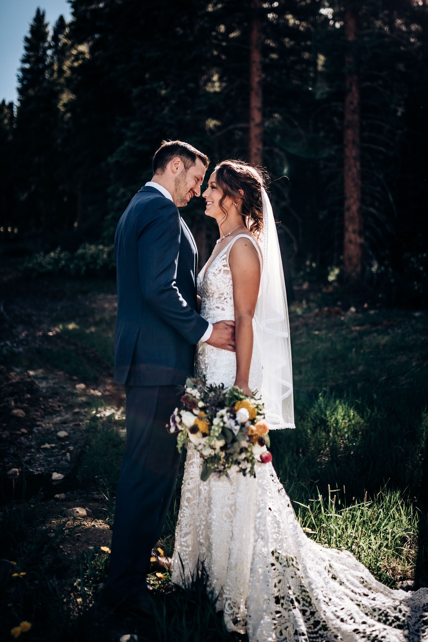 An intimate wedding portrait against a forest backdrop during golden hour.