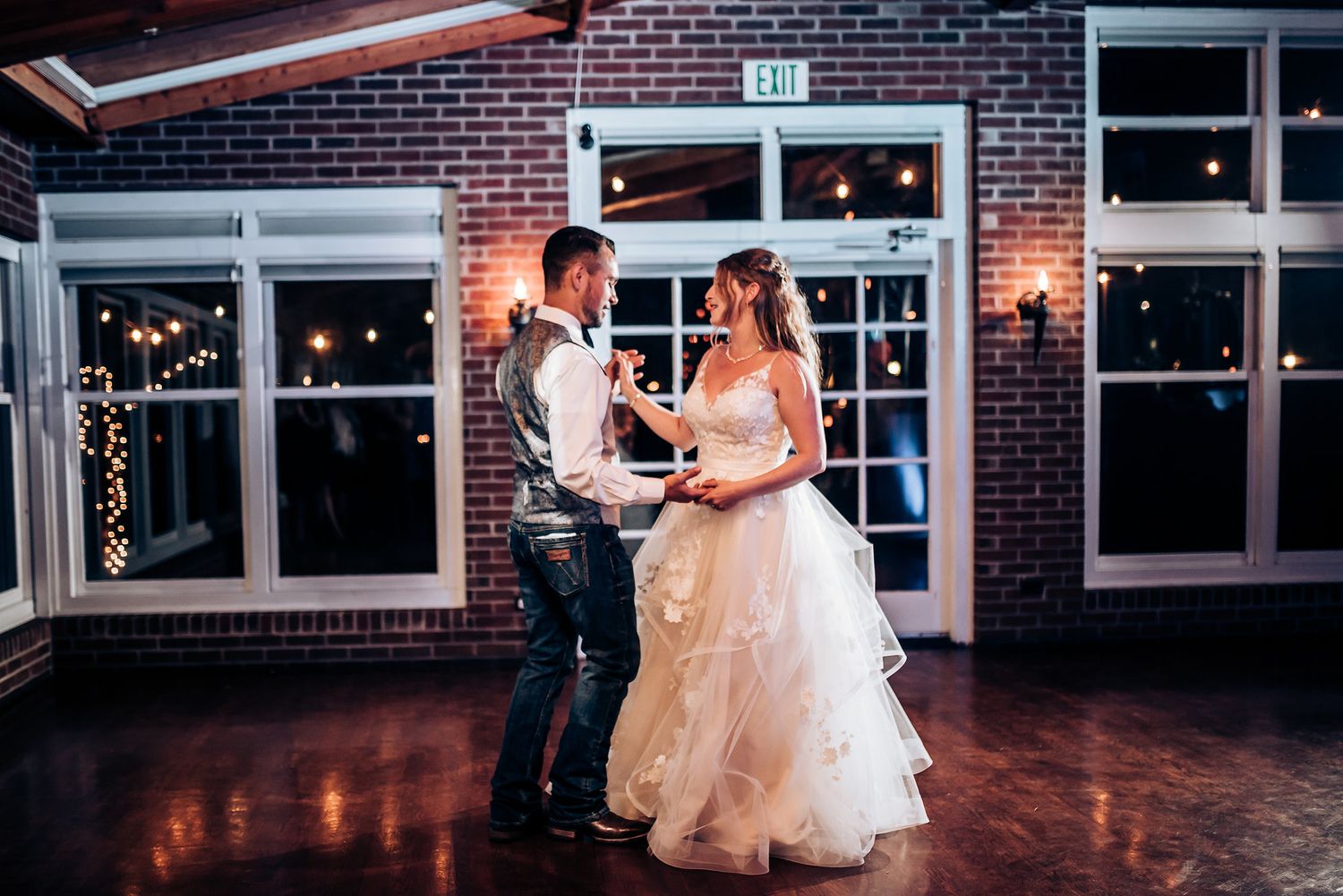 Couple dances together at their reception in a rustic brick venue with warm lighting.