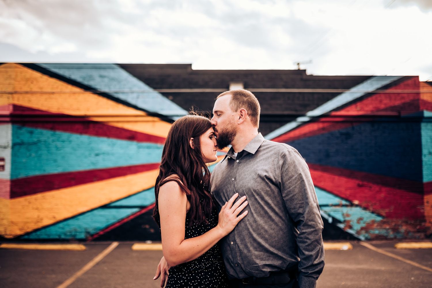 A romantic couple shares an intimate moment in front of a colorful geometric mural.