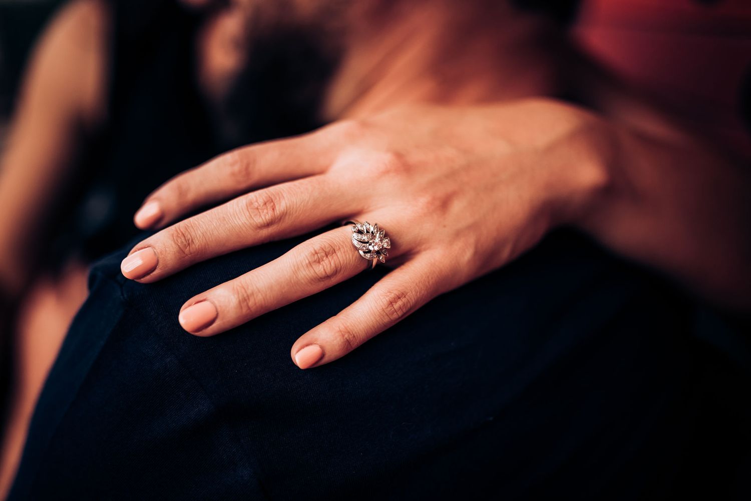 A close-up of a hand wearing a sparkly engagement ring.
