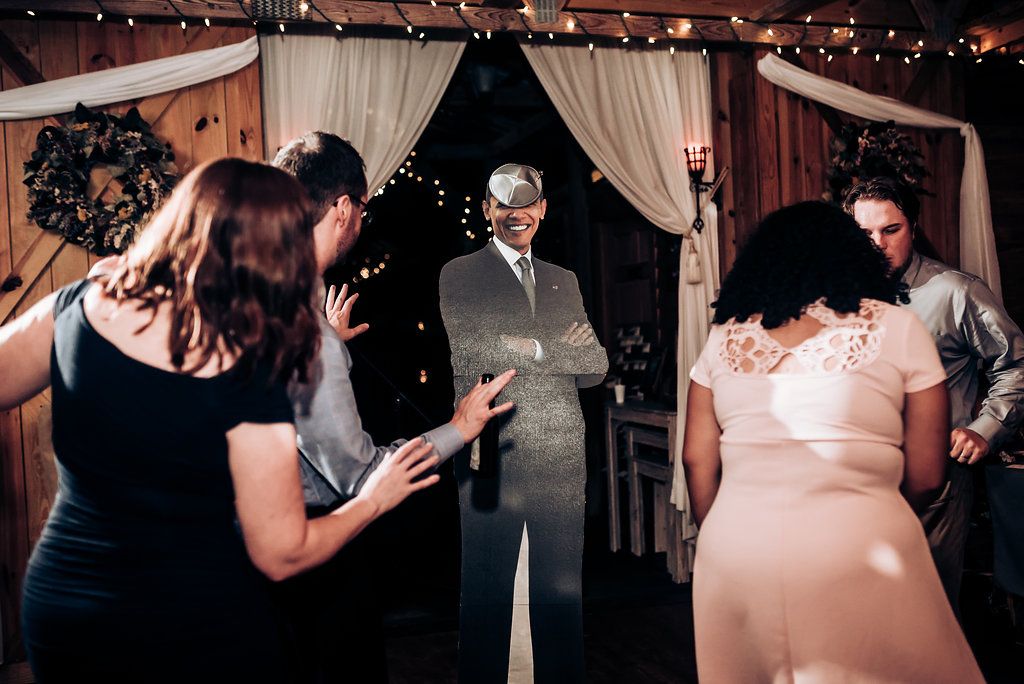 Wedding guests gather for a special moment during the reception under draped fabric and string lights.