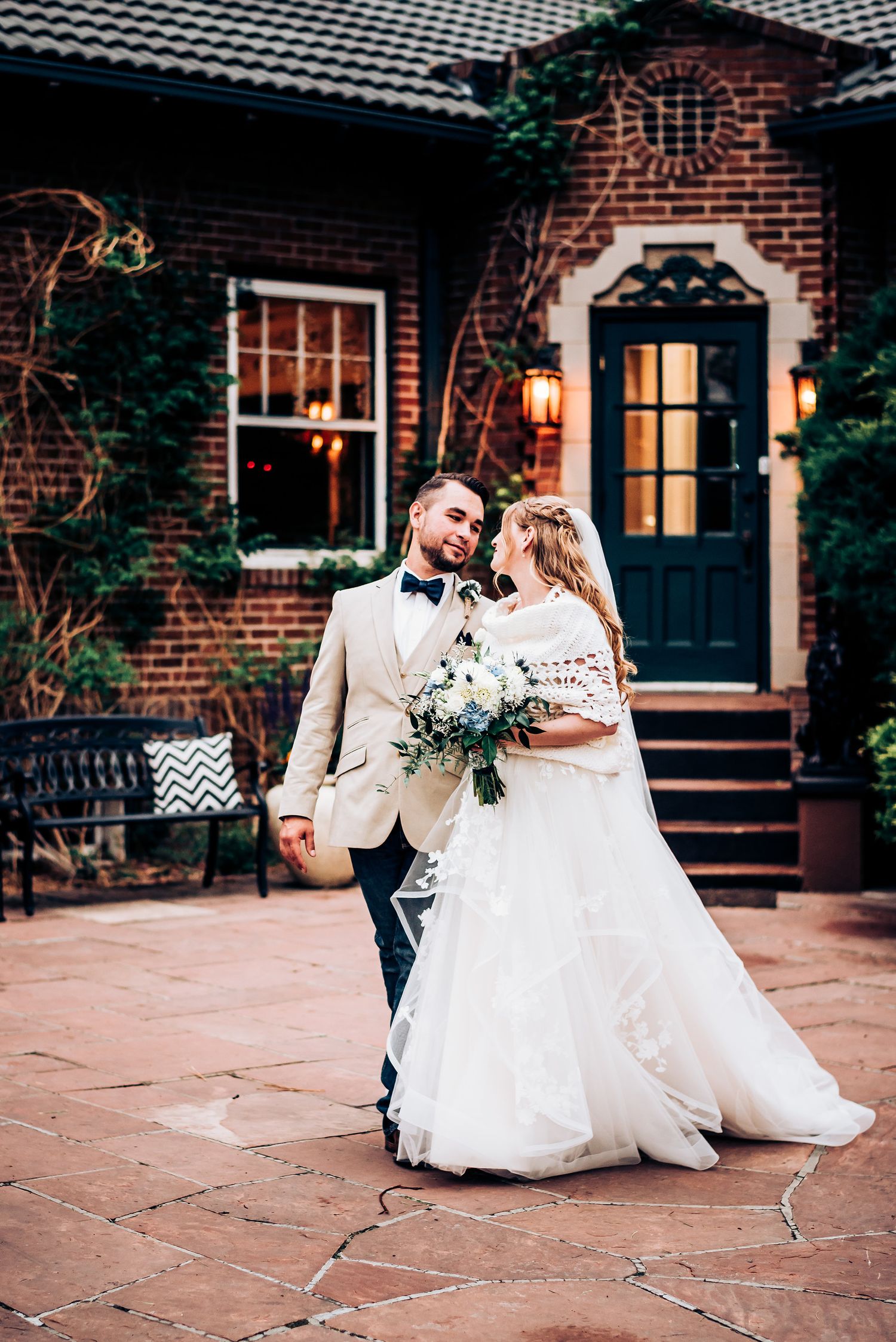 Candid wedding moment on terra cotta tiles with charming brick house backdrop.