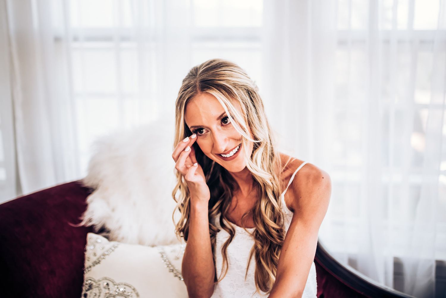 Person with wavy blonde hair sitting on couch laughing while talking on phone.