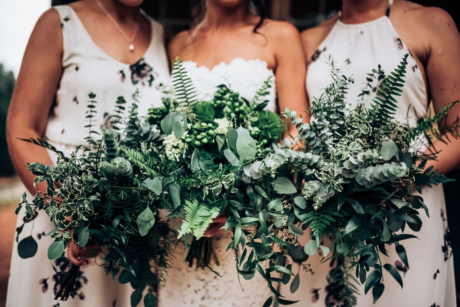 Row of green and white wedding bouquets with eucalyptus and ferns held by attendants.