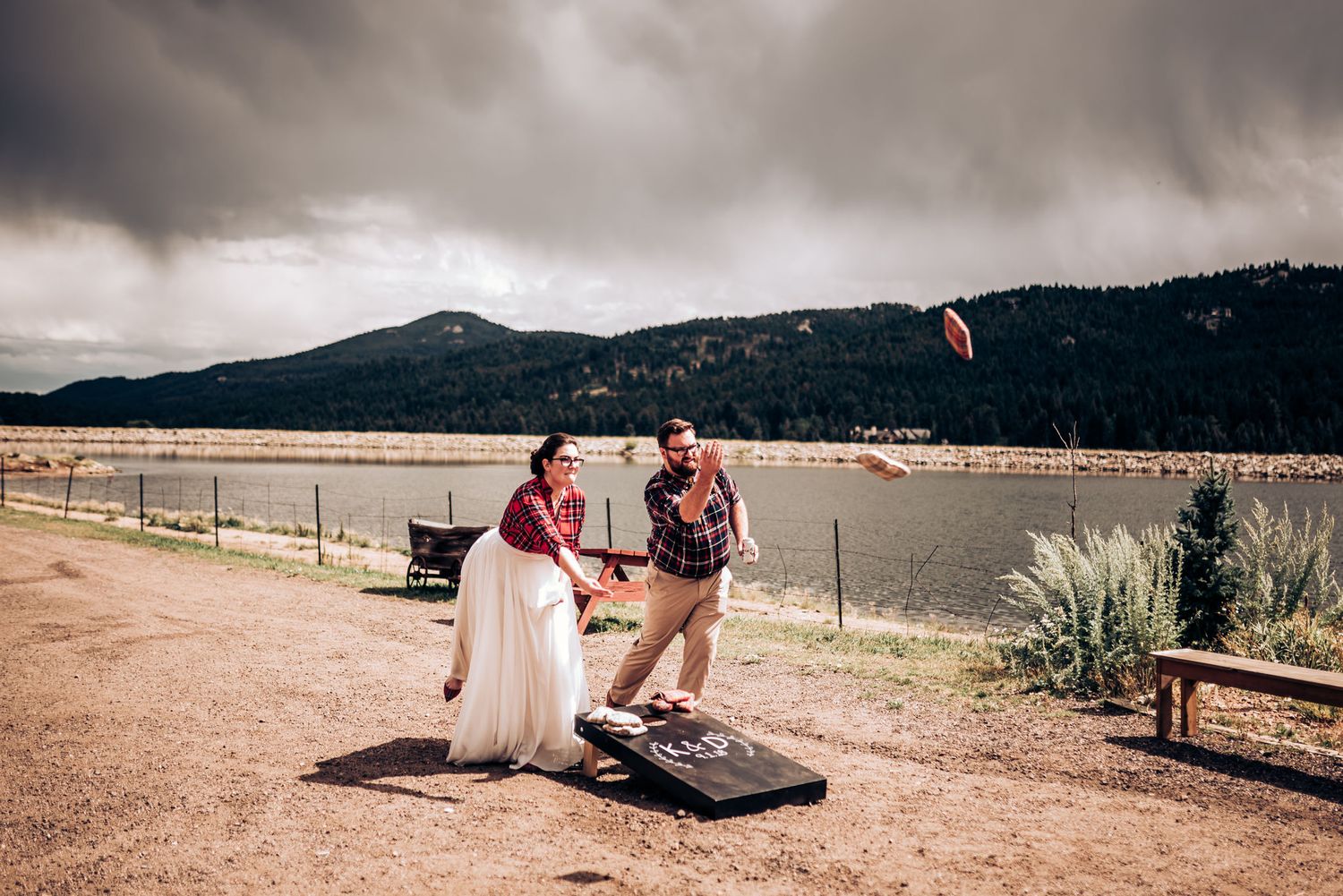 Two people enjoying a game of cornhole by a scenic mountain lake.