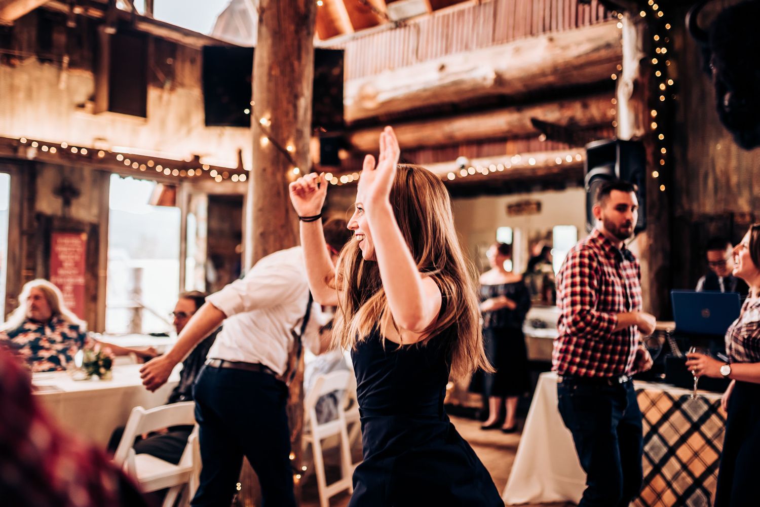 People dancing and celebrating at rustic barn wedding reception with string lights.