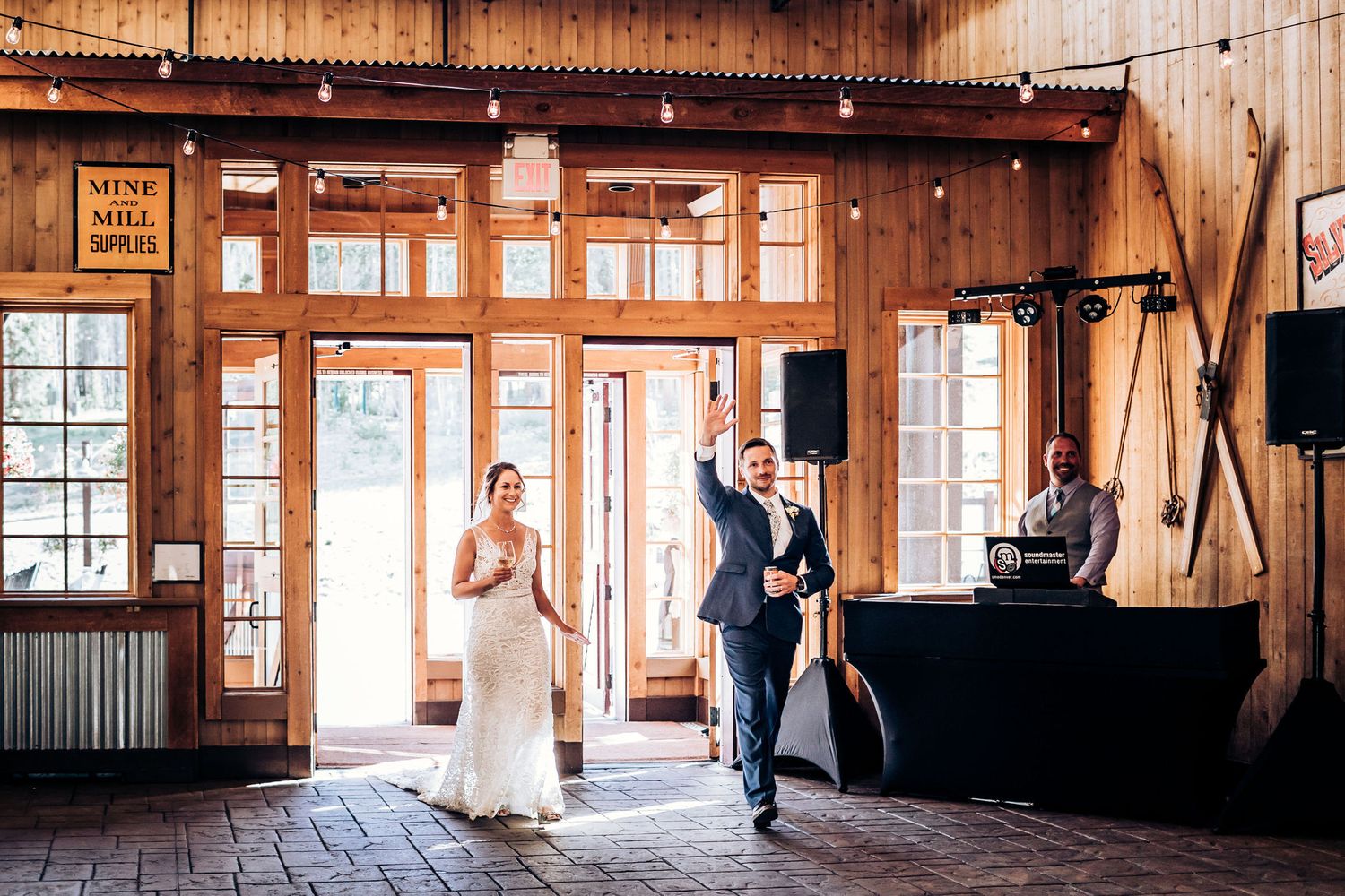 Couple entering a rustic wooden venue with large windows and natural lighting.