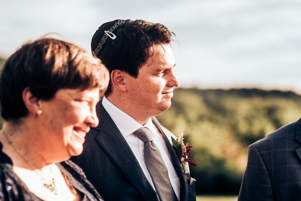 Wedding attendees stand together during an outdoor ceremony against a scenic backdrop.