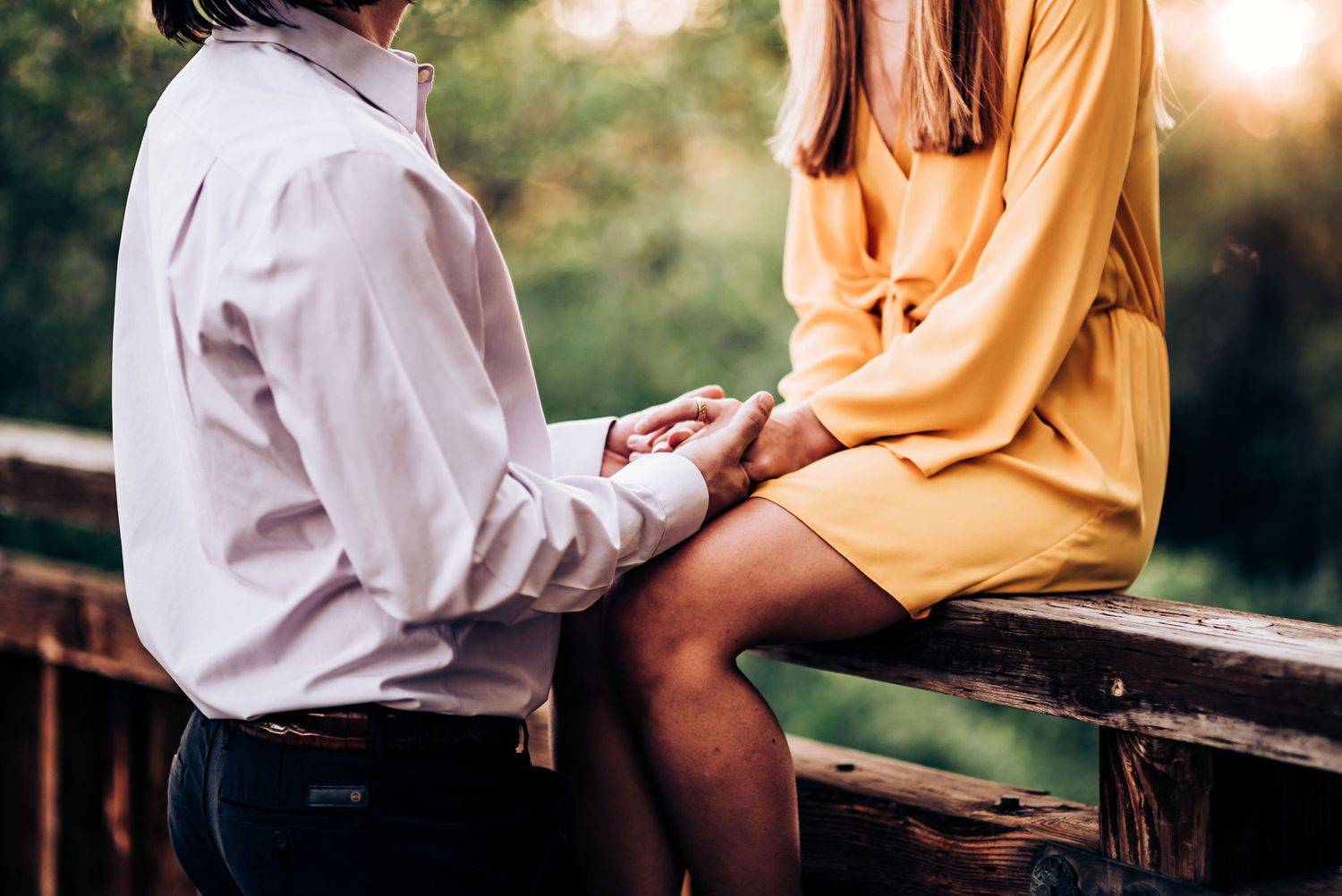 A couple shares an intimate moment while sitting on a wooden bench in nature.