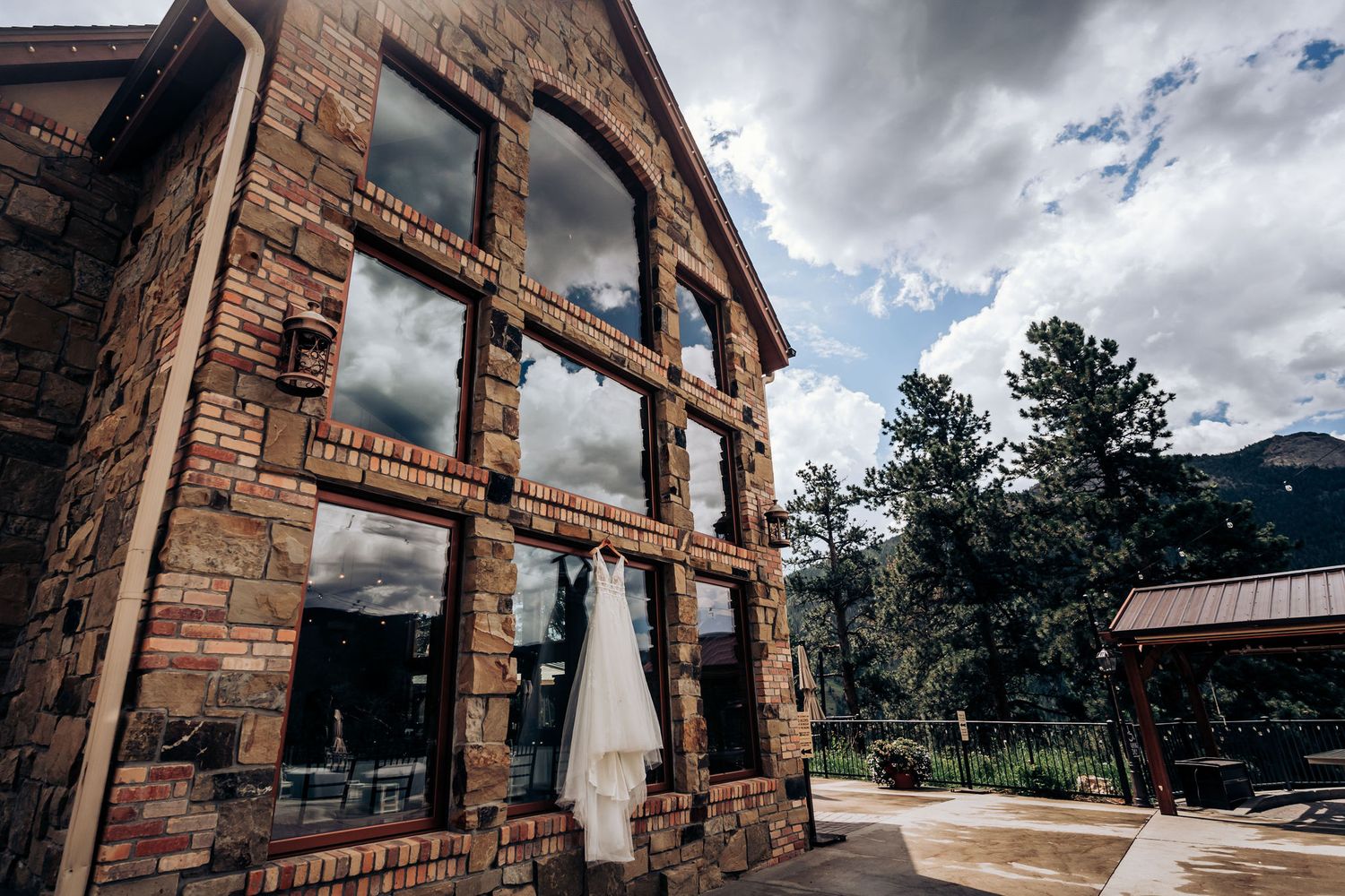 A rustic brick building with large windows and a white dress displayed in the foreground.