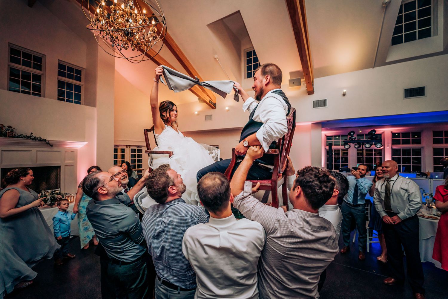 Wedding couple hoisted above crowd during traditional chair dance at reception.