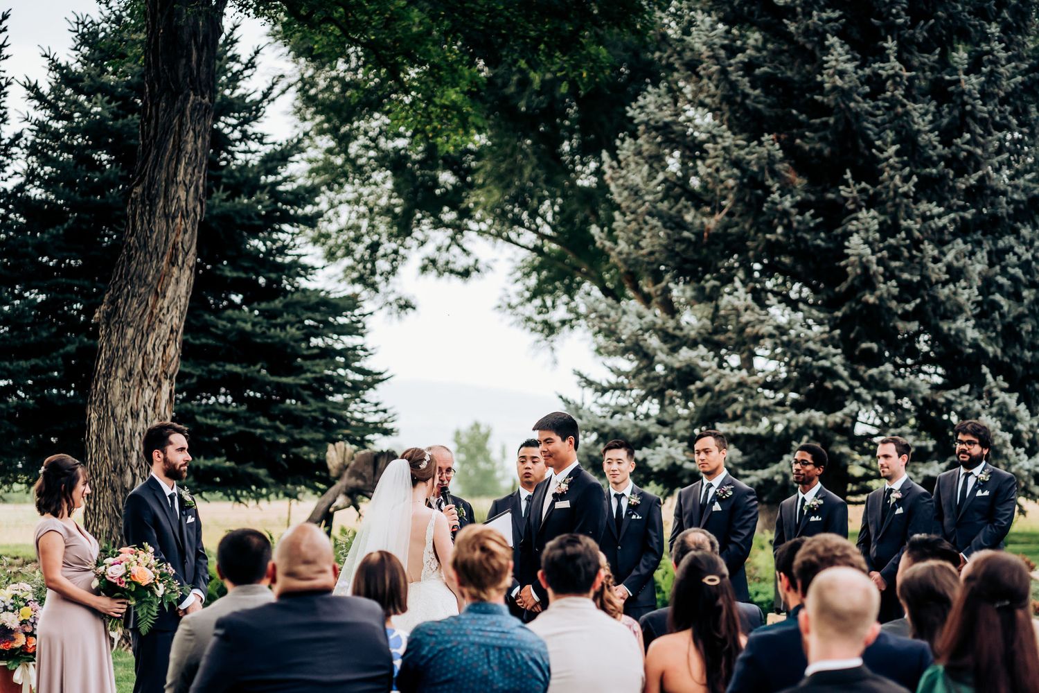 Wedding ceremony taking place outdoors with evergreen trees and mountains creating a scenic backdrop.