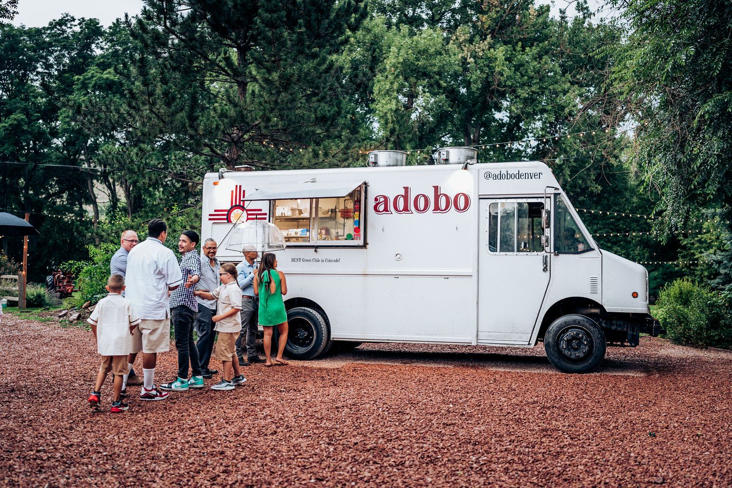 Customers gathering around a white food truck labeled 'adobo' parked on gravel.