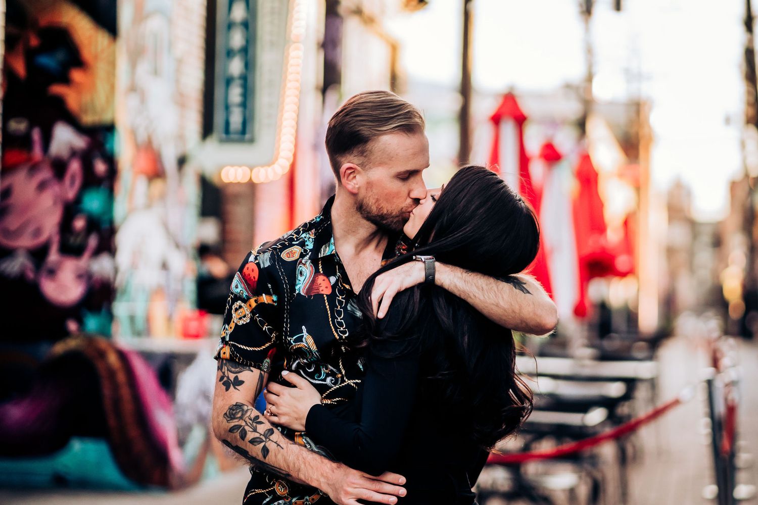 A couple shares a romantic moment in an urban setting with street art and sunset lighting.