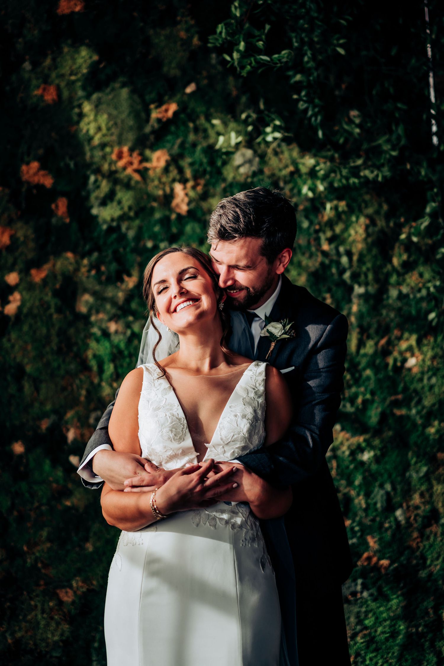 Intimate moment between newlyweds embracing against lush garden backdrop.