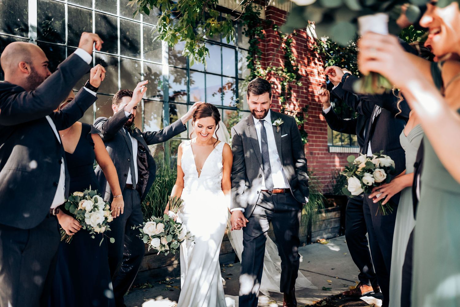 Wedding exit celebration as guests toss petals in bright sunlit venue.