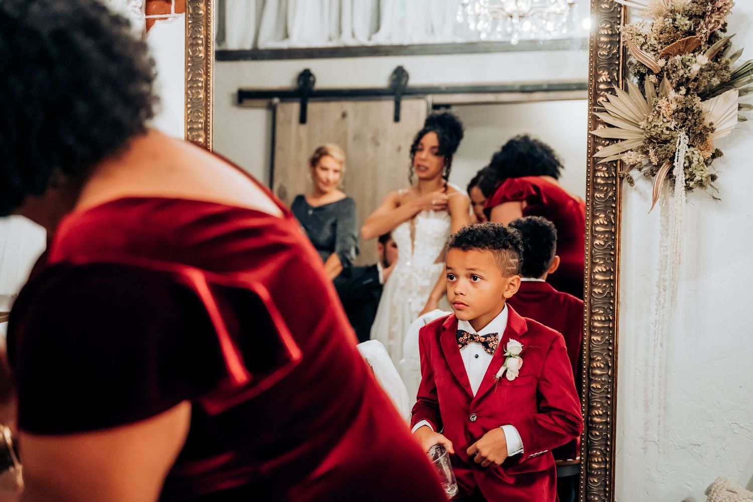 Young attendee in red suit admiring reflection in mirror during wedding preparations.