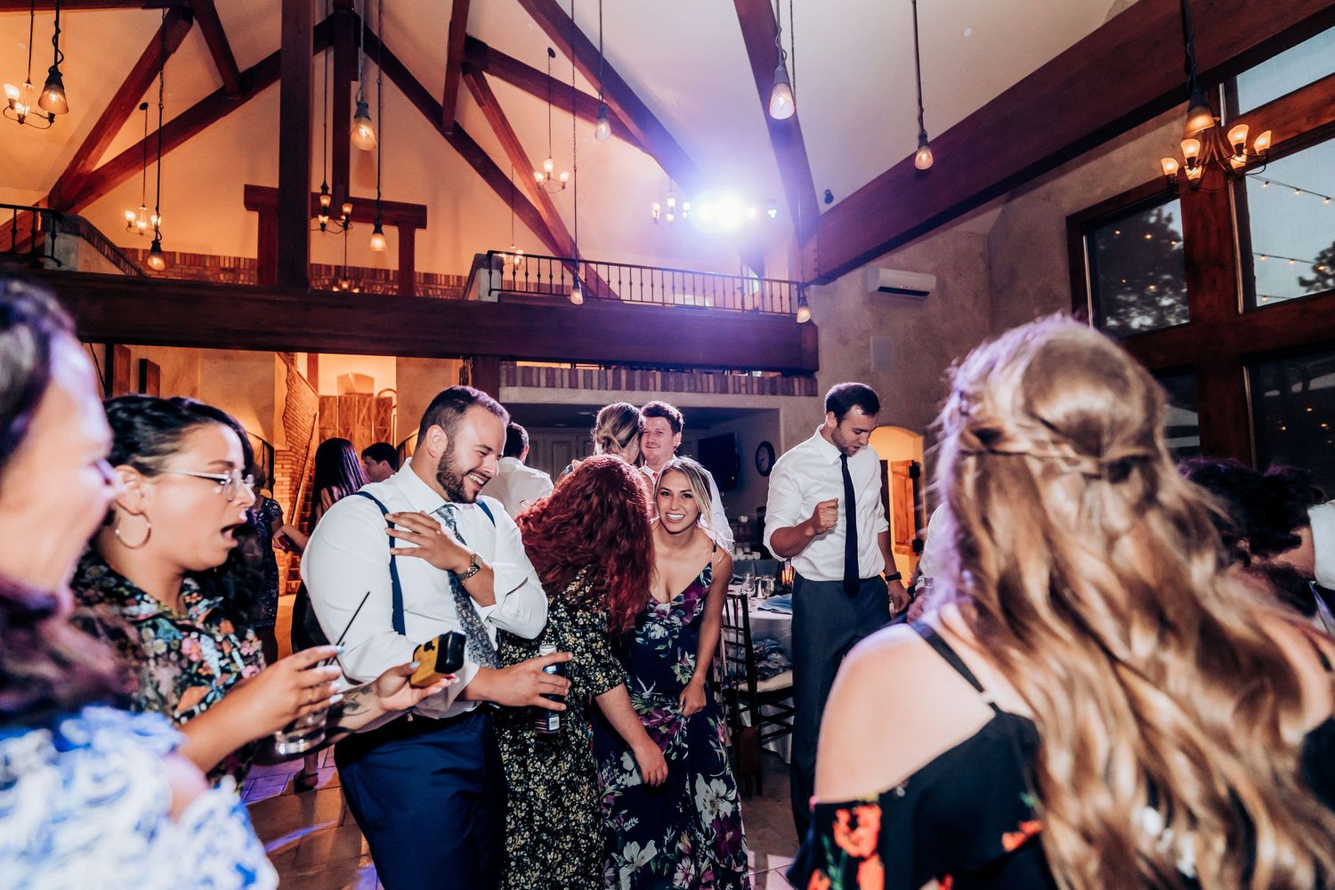 Wedding guests dancing and celebrating on a dance floor in a rustic venue with exposed wooden beams.