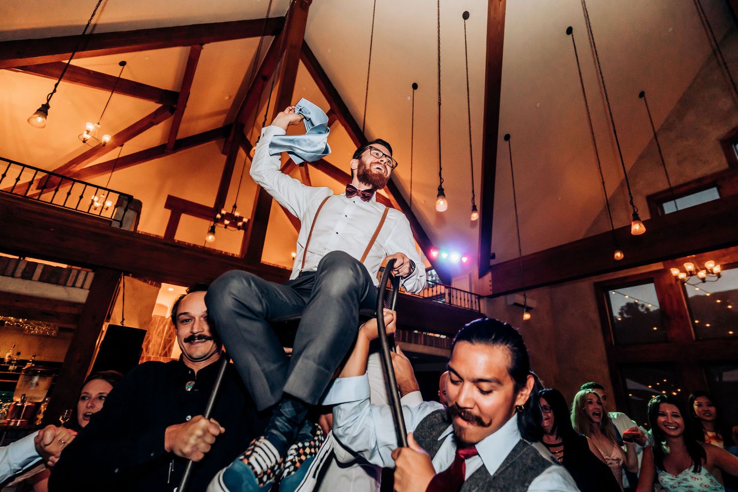 Partygoers hoist a guest into the air during an energetic wedding celebration indoors.