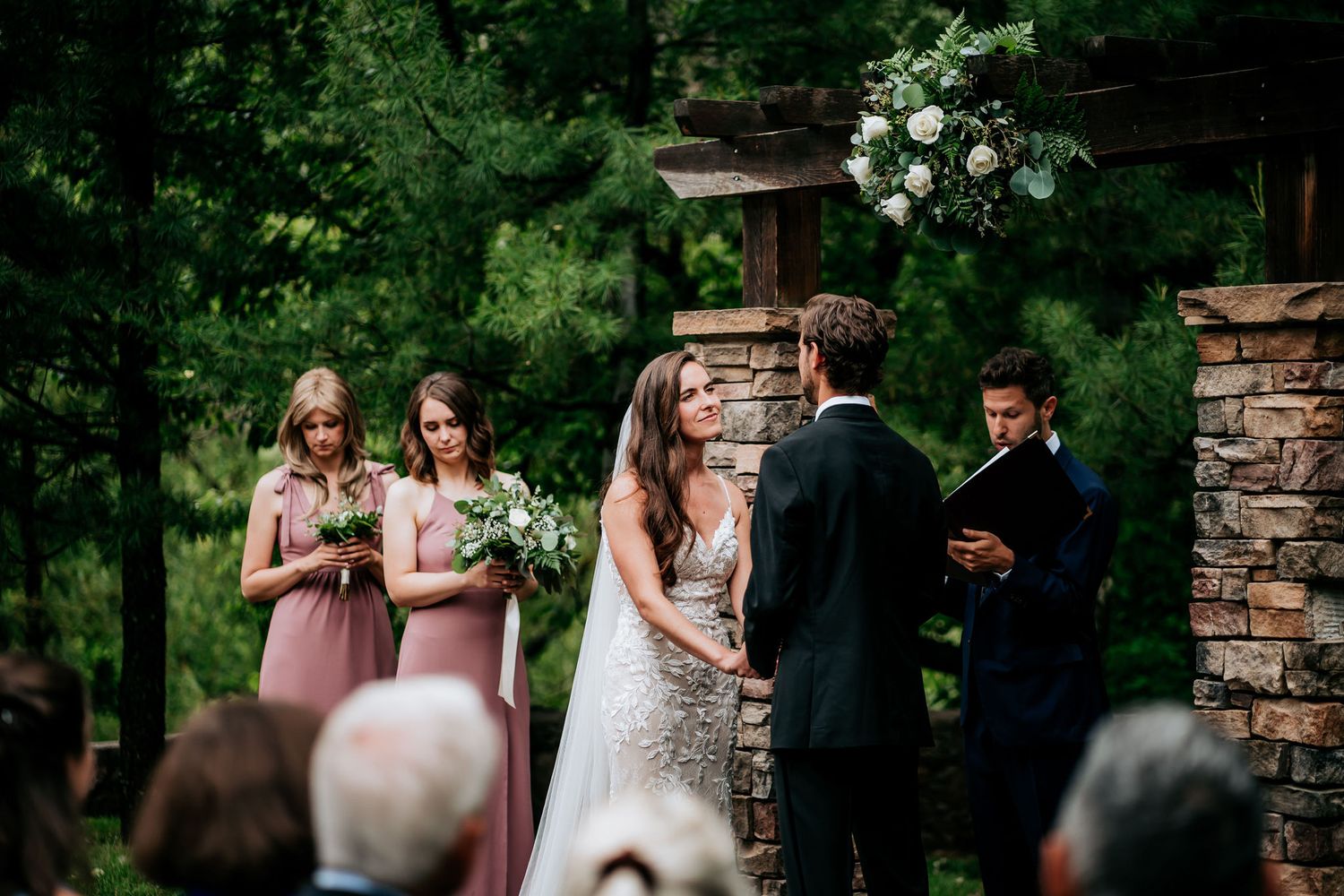 Outdoor wedding ceremony with stone pillars and floral arrangements in a forest setting.