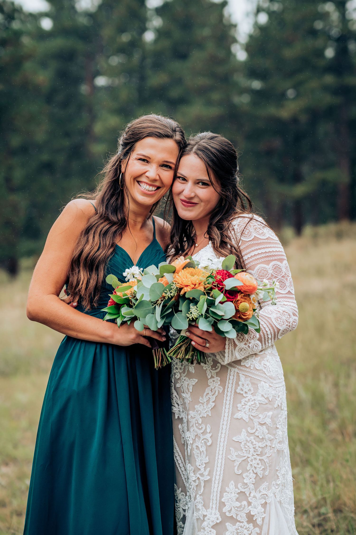 Two attendants pose with a vibrant floral bouquet against a mountain backdrop.