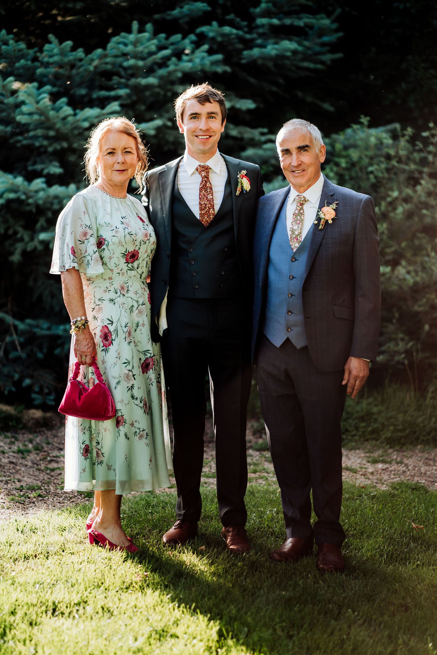 Family portrait at an outdoor wedding with mint floral dress and navy suits in a garden setting.