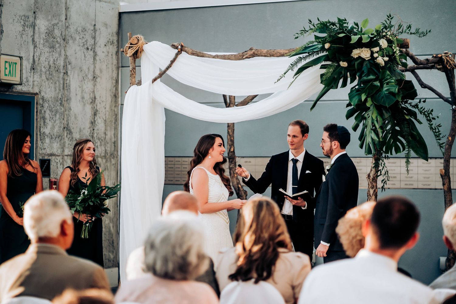 Intimate wedding ceremony moment under white draped arch with greenery.
