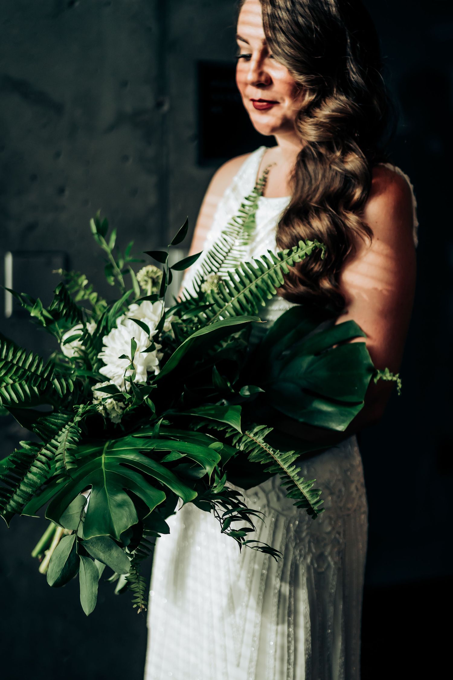 Elegant figure holding a lush tropical greenery bouquet against dark background.