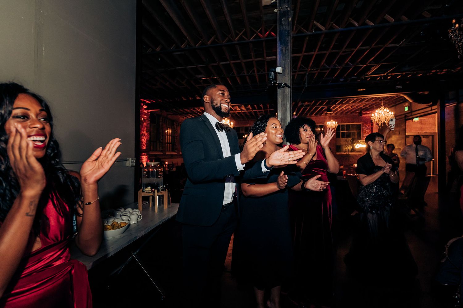 Wedding guests clap and celebrate during reception party with red dress accent.