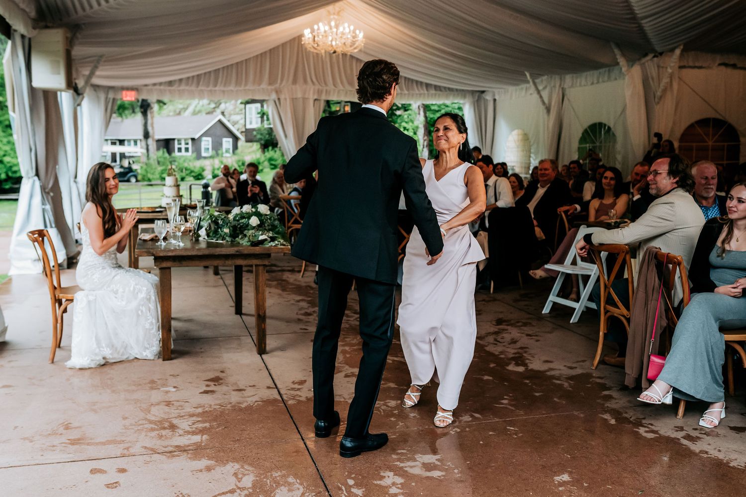 Wedding couple dancing under a white tent reception space surrounded by seated guests.