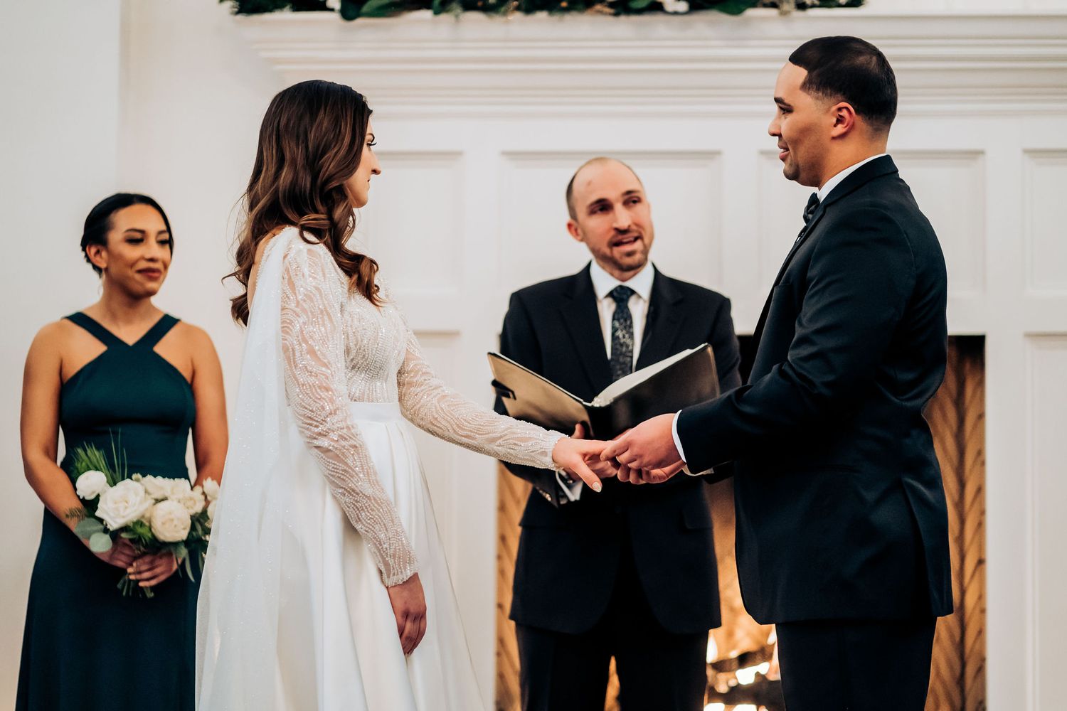 An intimate wedding ceremony moment as the couple exchanges vows in front of an elegant fireplace.
