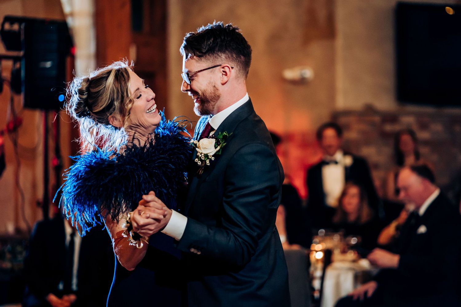 A mother and son dance together with dramatic blue feather accents at a wedding reception.