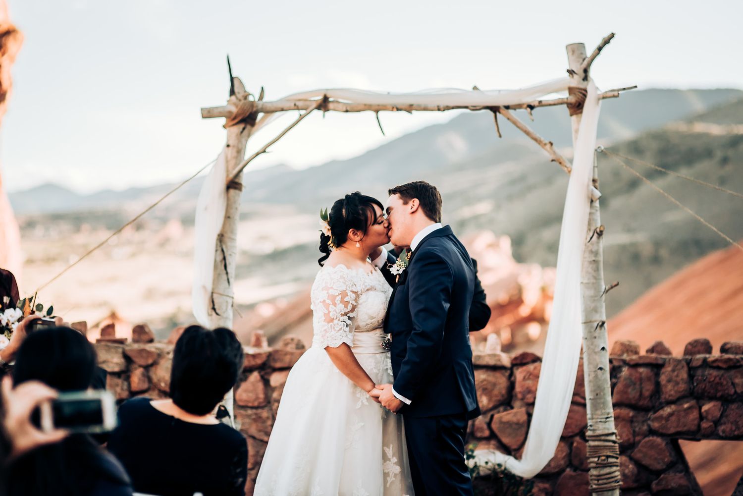 Couple exchanges vows under a handmade arch with dramatic red rock landscape behind them.