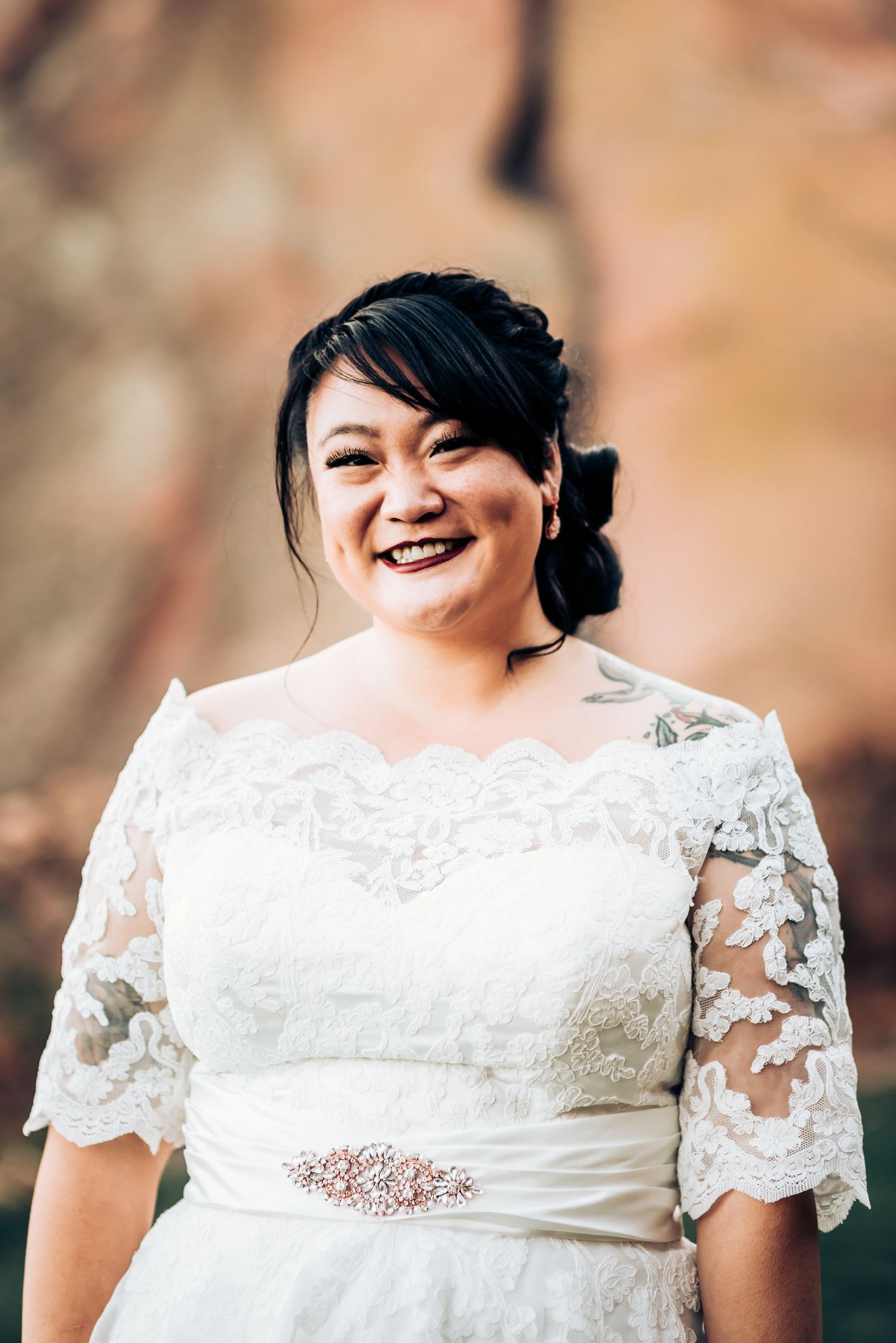 Elegant bridal portrait featuring white lace dress with crystal belt detail against natural backdrop.