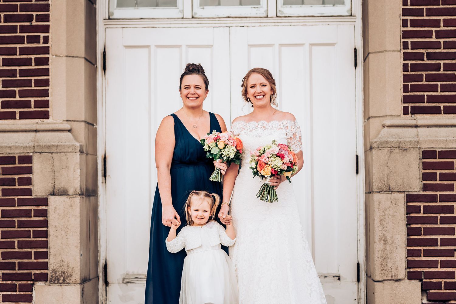 A sweet wedding portrait with navy blue bridesmaid dress and white gown against church doors.