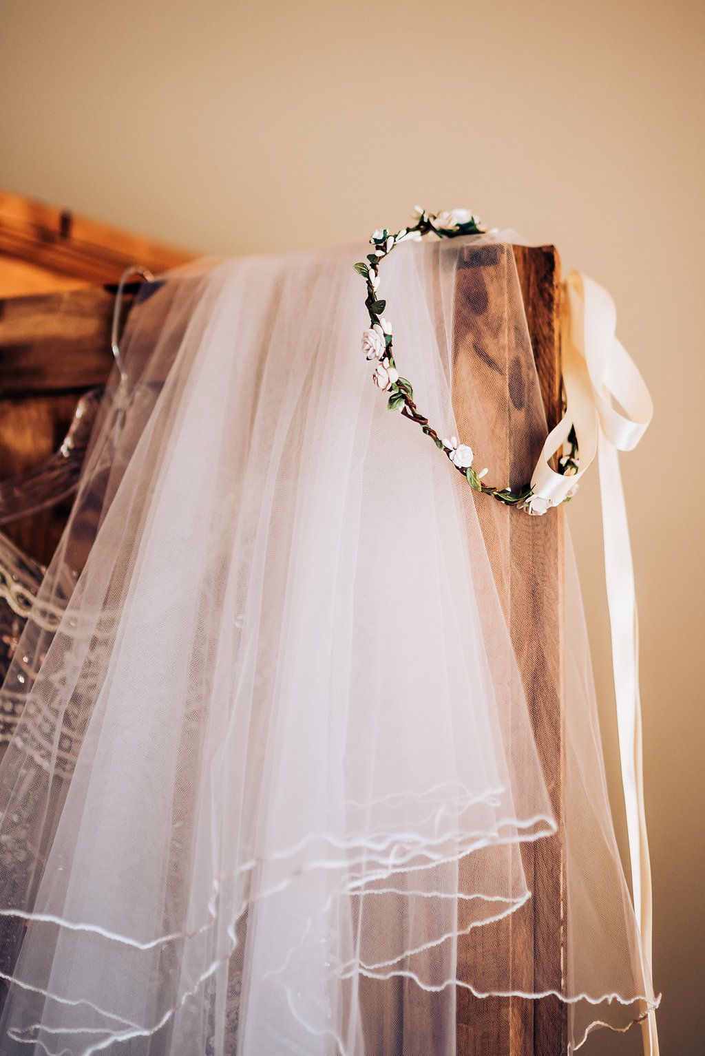 A delicate white wedding veil hangs elegantly with a floral crown headpiece displayed on a wooden surface.