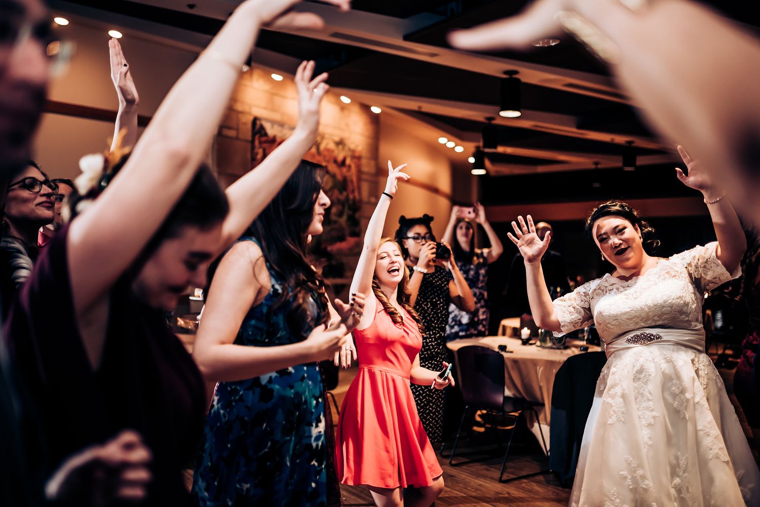 Wedding reception guests dancing with arms raised during a celebration.