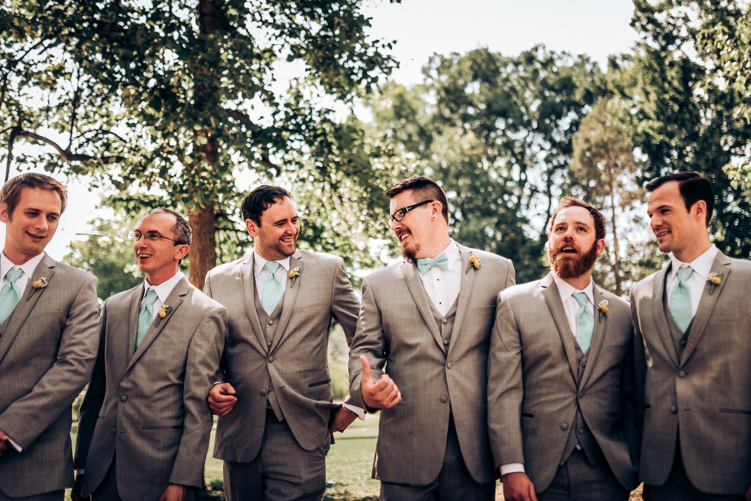 A group of groomsmen in matching gray suits posing together outdoors.