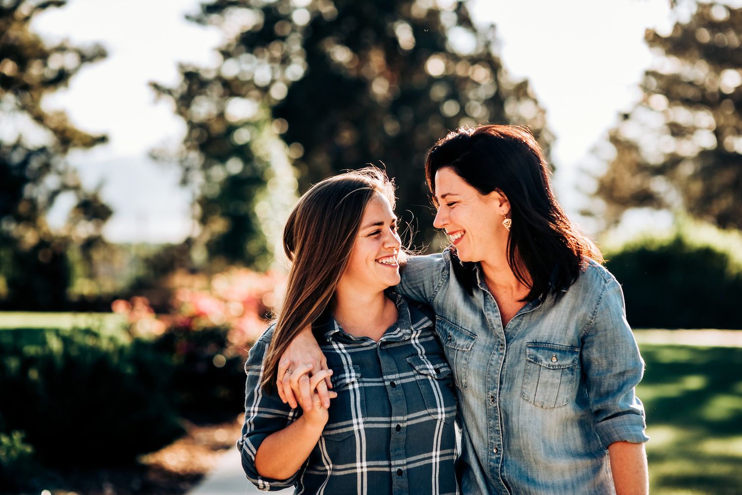 Two people share joyful laughter while standing together in a sunny garden.
